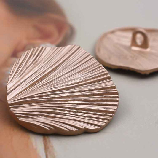 Gold leaf metal button with ridged striped pattern, detailed close-up