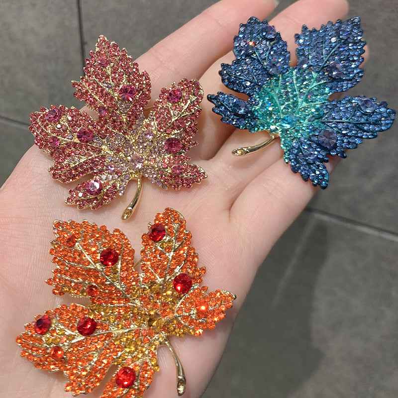Assorted maple leaf brooch pins in blue, orange, and rose with rhinestone sparkle