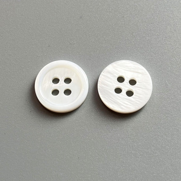 Round natural white pearl shell button, four-hole, textured front; two pieces shown