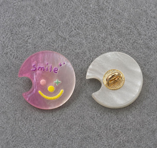 Pink moon-shaped resin shank button with colorful smiley face; gold back shank detail