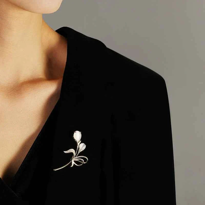 Small floral brooch on lapel, gold-tone design with beige cat’s-eye