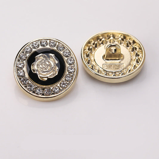 Runder Zierknopf mit goldfarbener Umrandung, Strasskranz und Blumenmotiv vor dunklem Einsatz