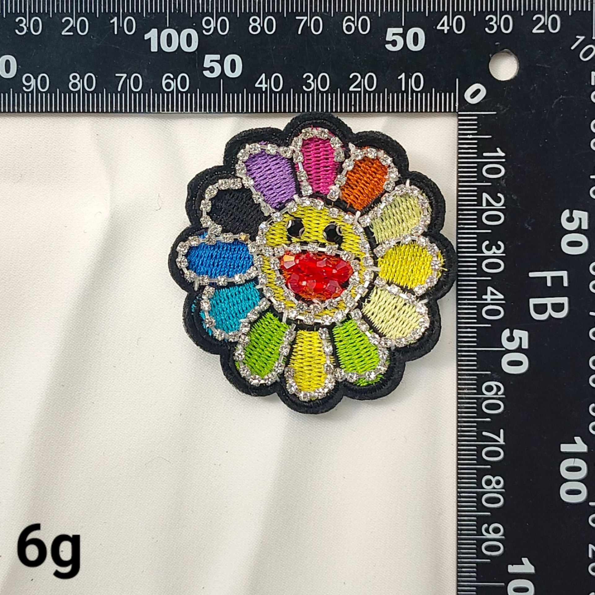 Parche girasol bordado con pétalos multicolor y cristal rojo central, vista cercana.