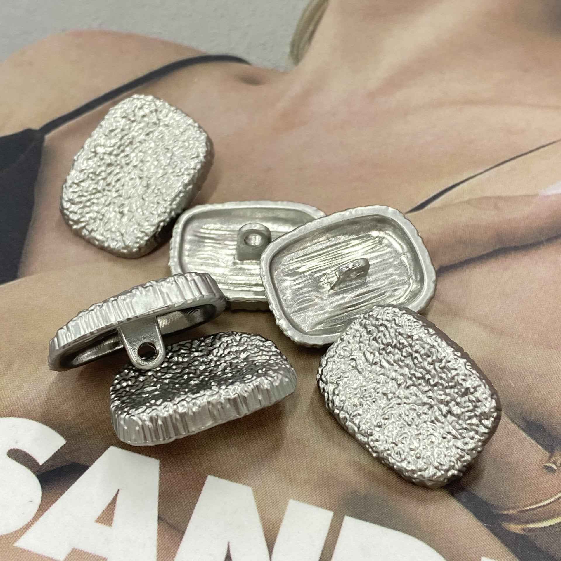 Silberfarbene Metallknöpfe mit Stiel, rechteckig, sichtbare Befestigung, geprägte Textur
