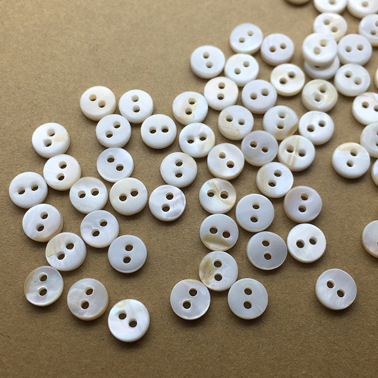 Natural white 2-hole mini round shell buttons, scattered on a tan surface (40 pcs)