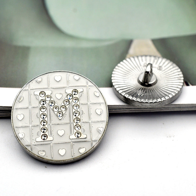 White round button with rhinestone letter 'M' and small heart grid motif
