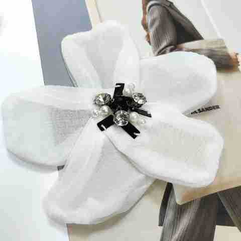White organza chiffon flower applique on fabric, with rhinestone center and black ribbon details