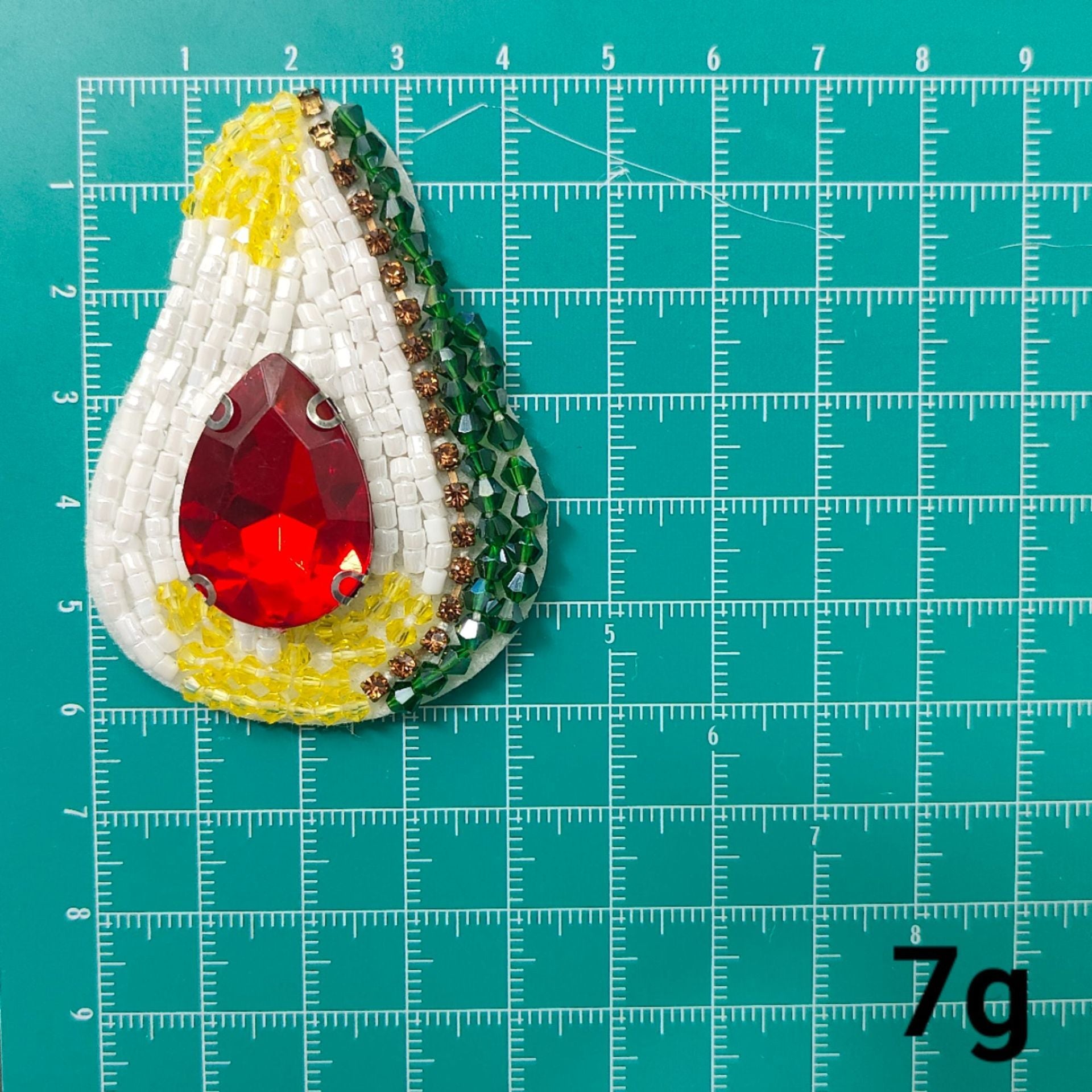 Parche tipo pera: bordado blanco y amarillo con pedrería roja en forma de gota