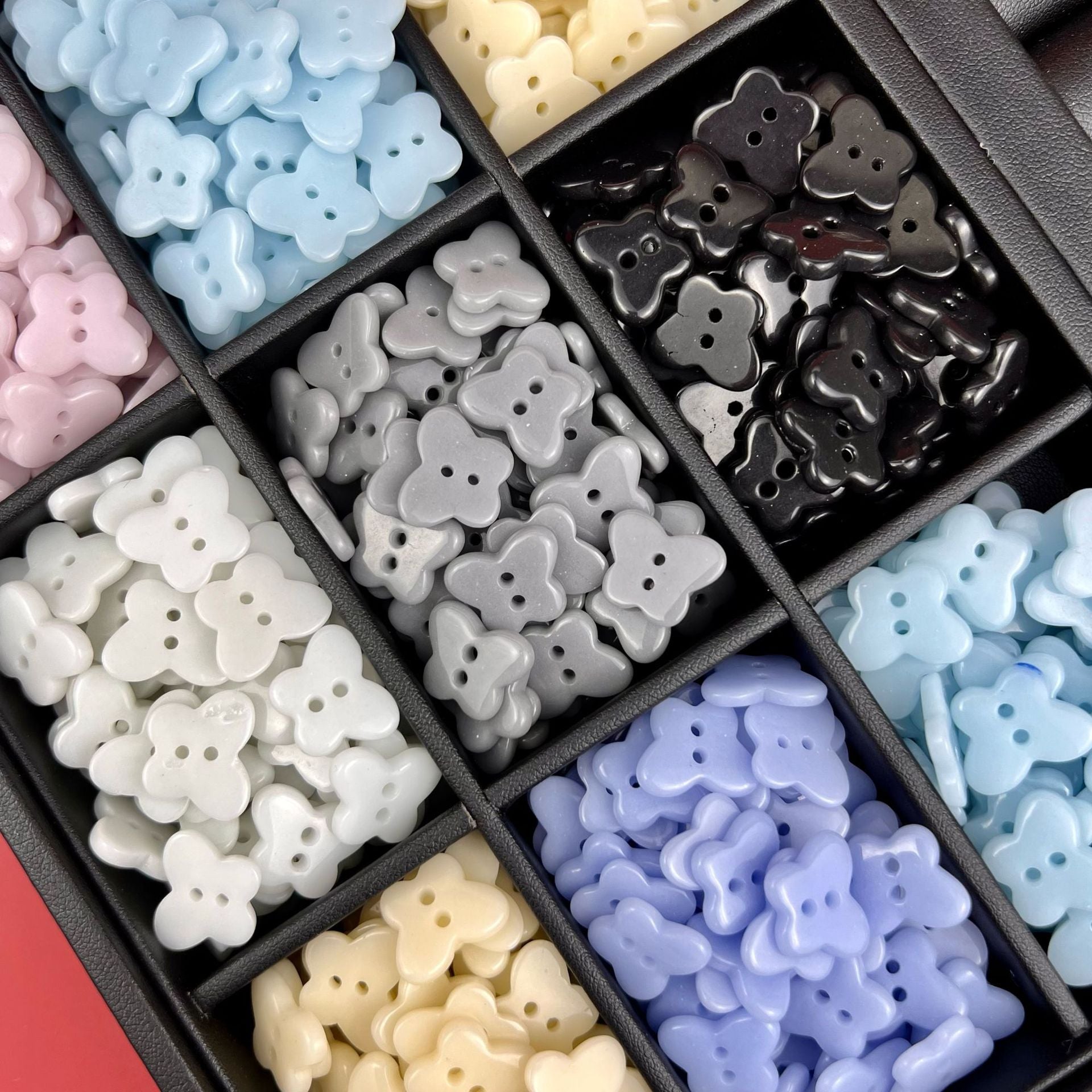 Ceramic butterfly buttons in a divided organizer: light blue, white, cream, purple, black, gray