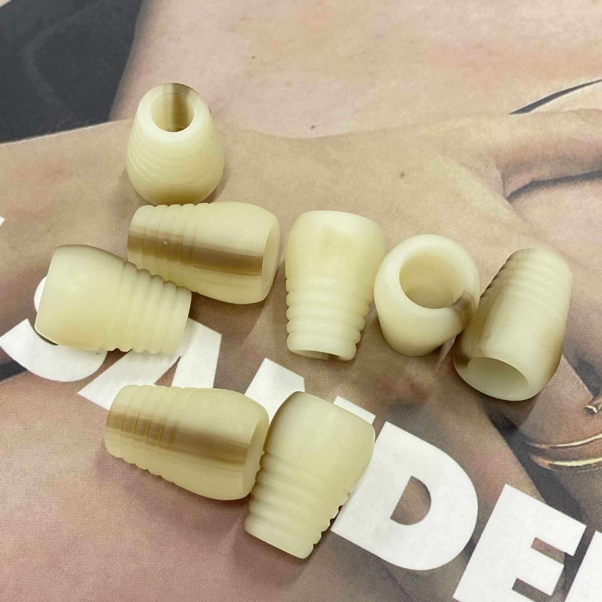 Ivory resin cord end stoppers with ribbed bell ends and a center hole