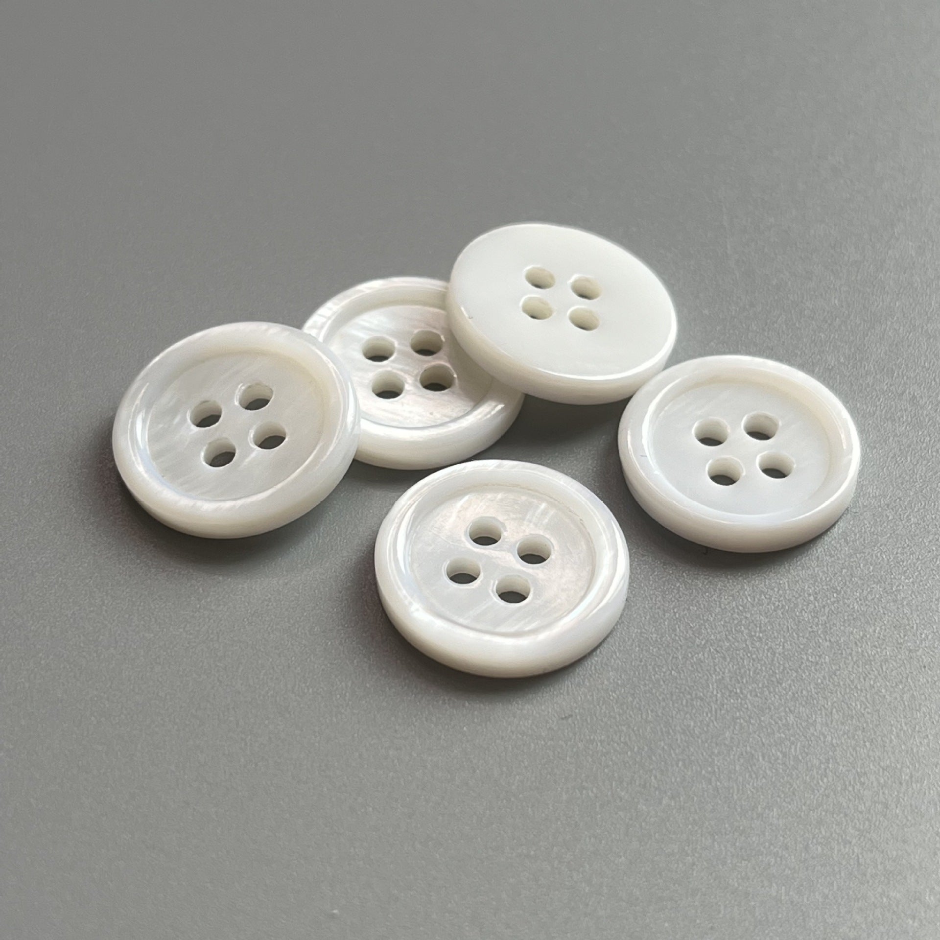 Round natural white pearl shell buttons, four-hole; five buttons arranged together