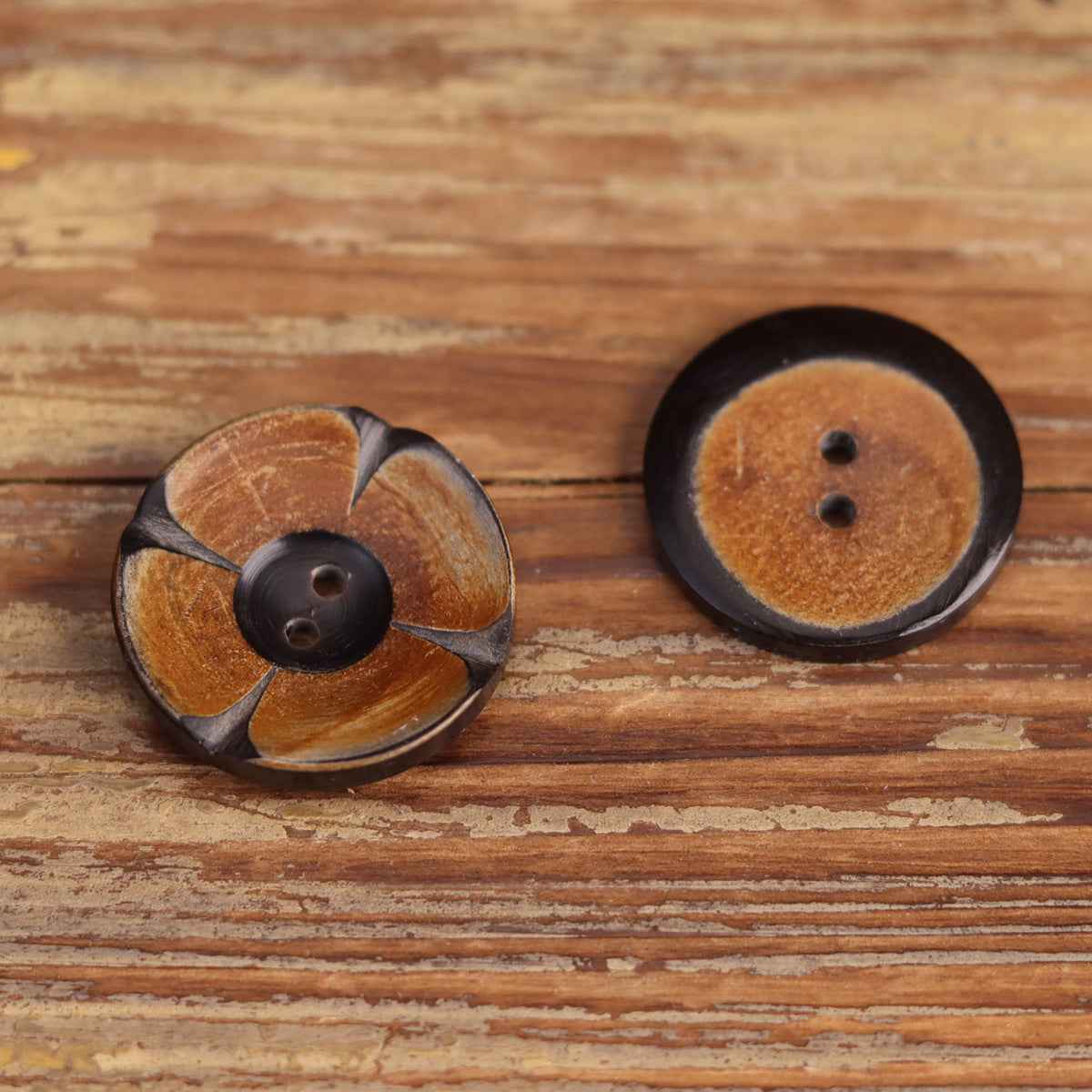 Two round 2-hole horn buttons with carved floral petals in mustard and dark tones