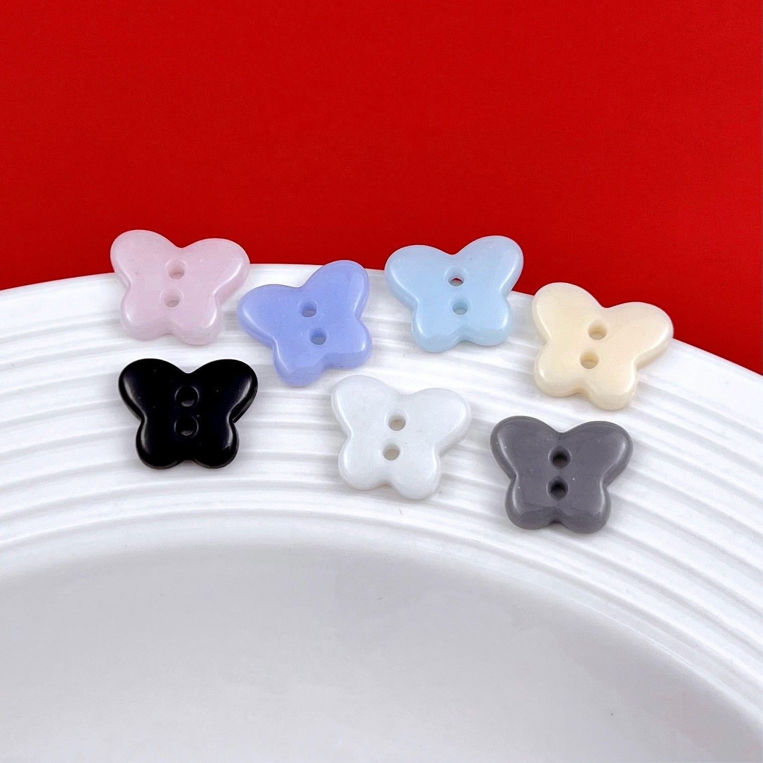 Butterfly ceramic buttons assortment on a tray: pink, light blue, pale yellow, black, white, gray