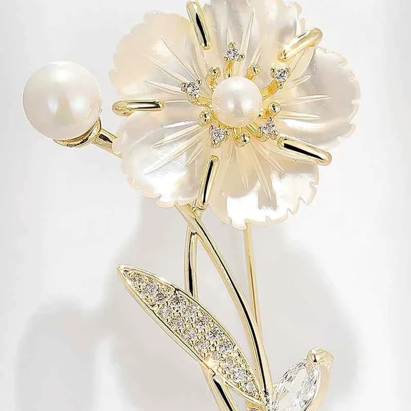 Close-up camellia brooch: white shell petals, center pearl, gold-tone leaf and stem