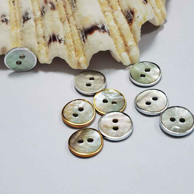 Two-hole round mother-of-pearl shell buttons with gold/silver edge, shown on fabric