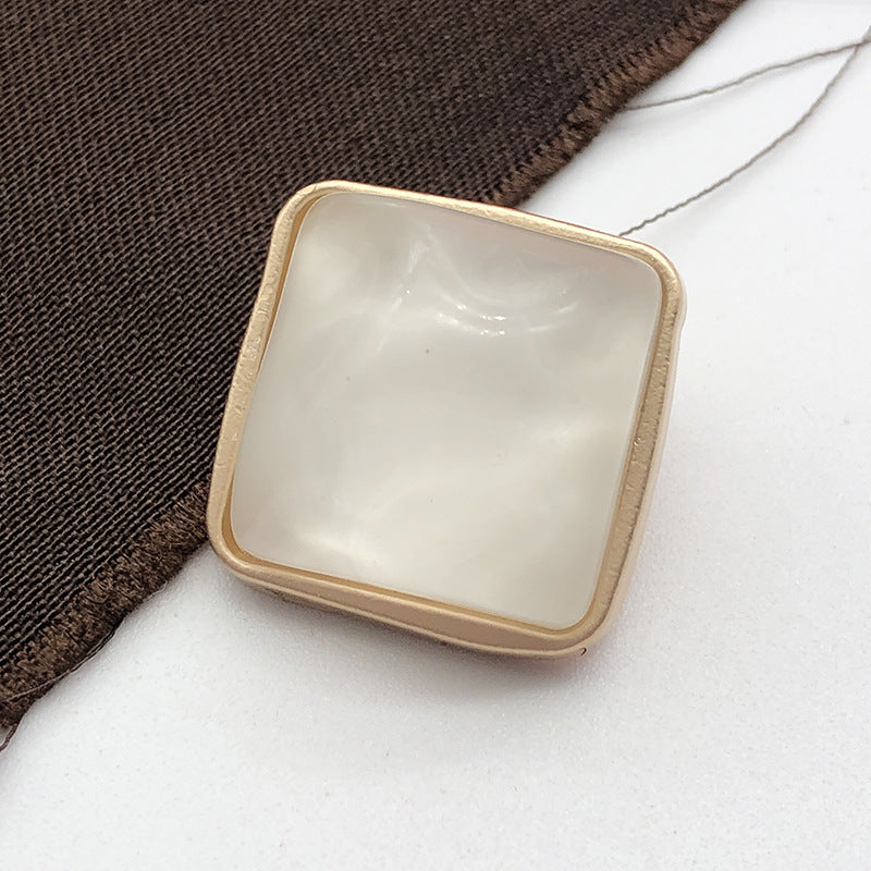 Square stone-look coat button, white/cream, gold-tone metal shank, close-up