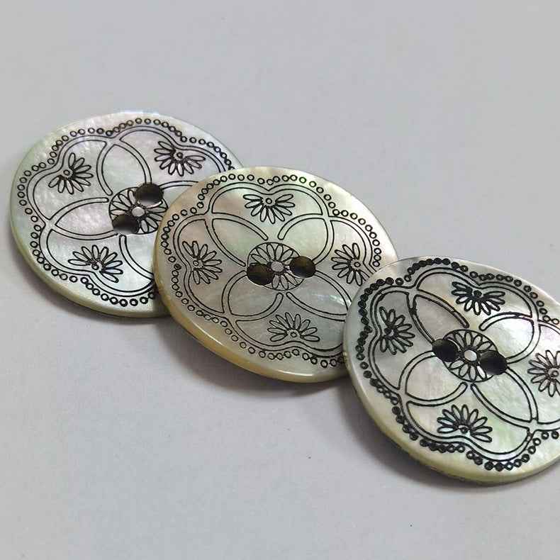 Three round mother-of-pearl 2-hole shell buttons with black floral motifs and dots