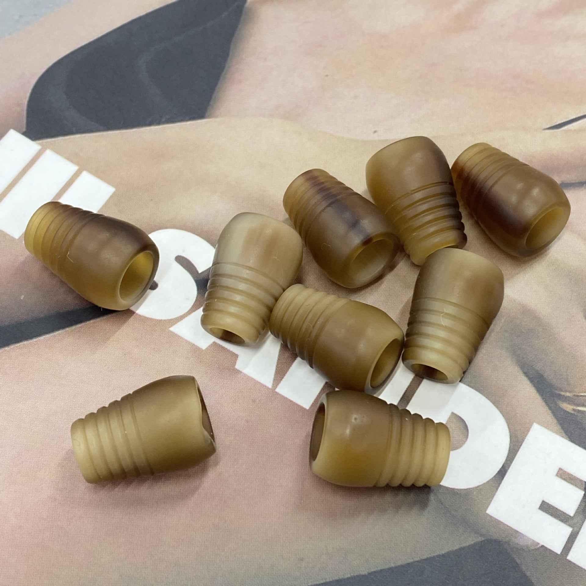 Tan and olive resin cord end stoppers with ribbed bell shape for hoodie strings