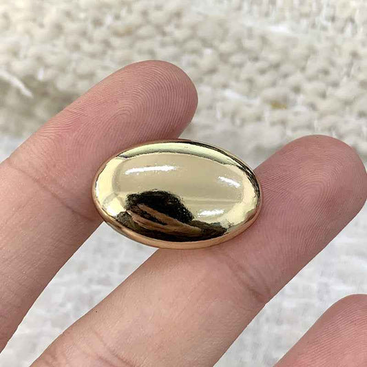 Oval light gold alloy shank button close-up, reflective domed front