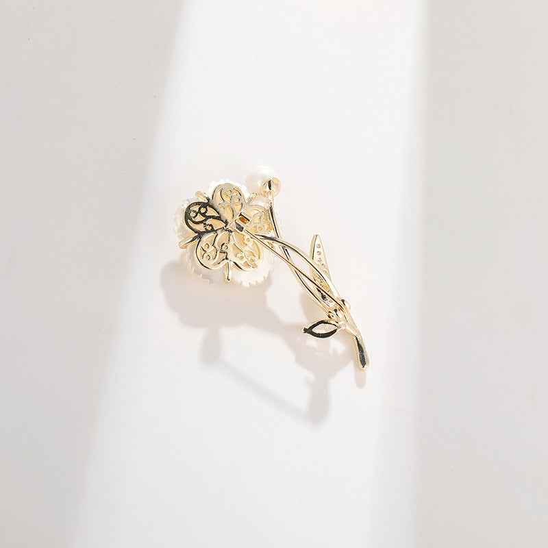 Floral camellia brooch pin with pearl center and gold-tone leaf detail, angled view