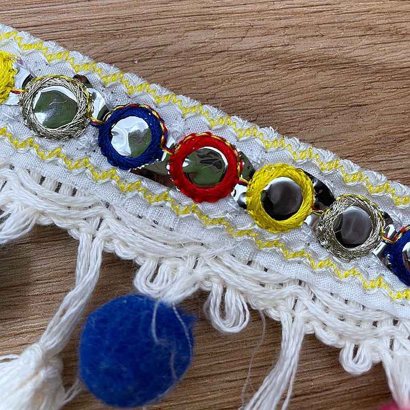 Close-up of colorful ring bead appliqués on white embroidered trim with yellow trim edge.