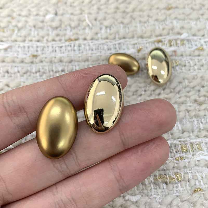 Two oval gold alloy shank buttons held in hand, domed fronts with shank posts
