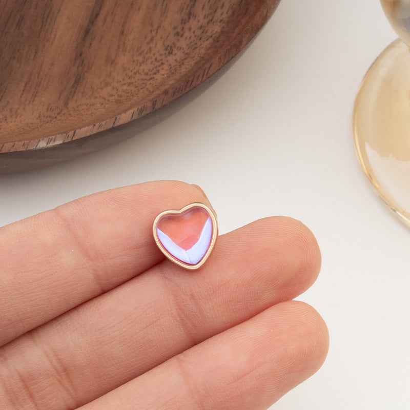 Heart-shaped button with pink-to-purple iridescent center and gold-tone edge, close-up