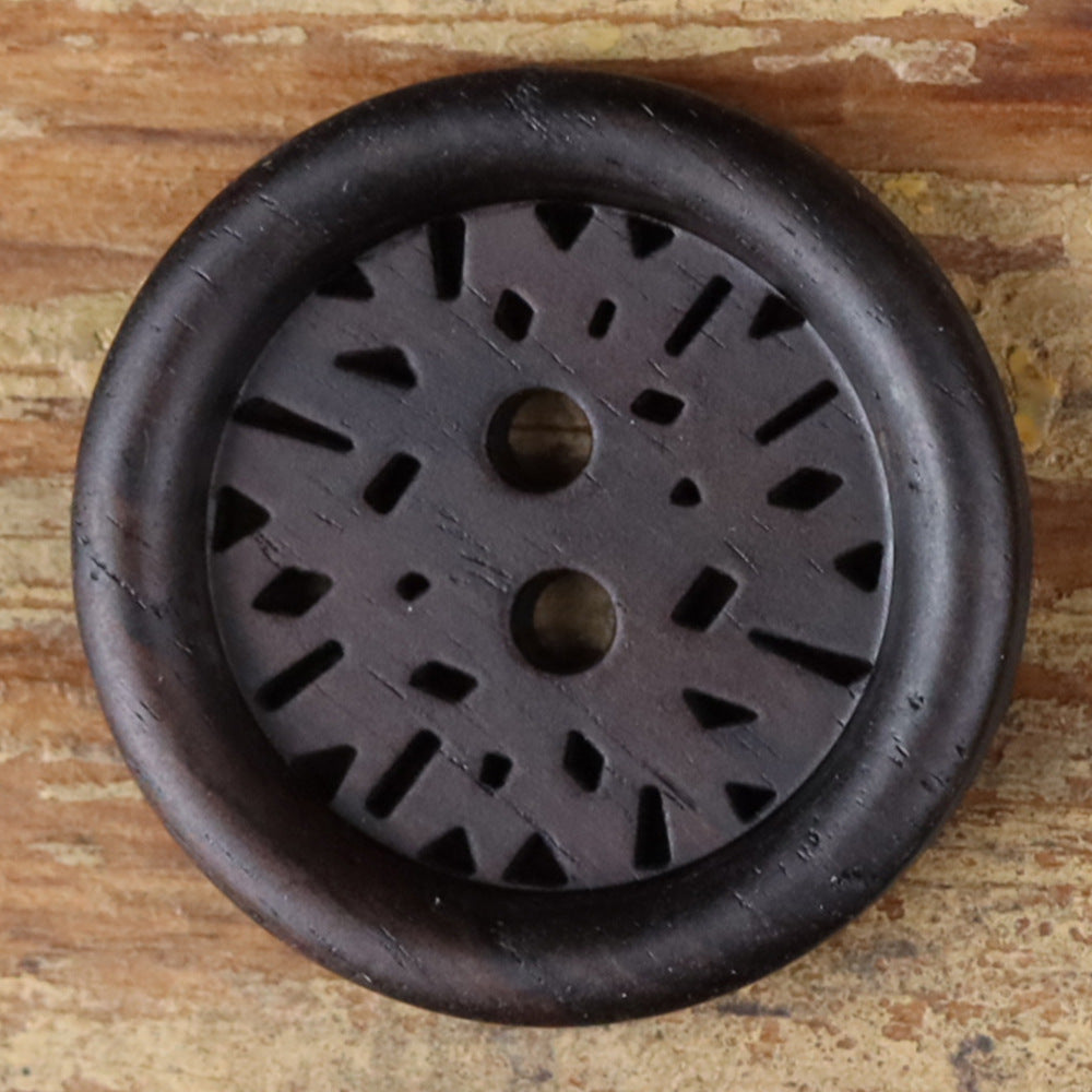 Close-up of round dark 2-hole coat button with laser-cut radial pattern