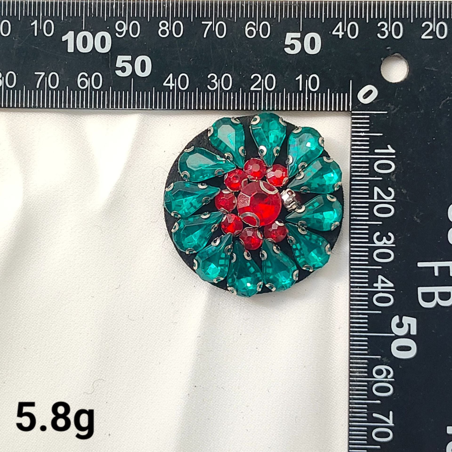 Teal round crystal patch with red flower center and gold-tone sparkle accents
