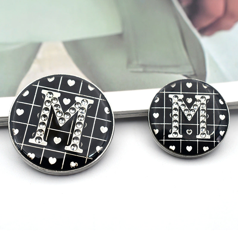 Black round button with rhinestone letter 'M' and small heart grid motif