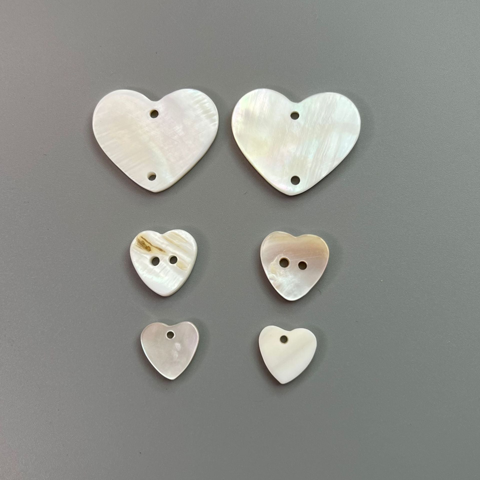 White heart-shaped shell buttons, 2-hole design, glossy pearlescent finish.