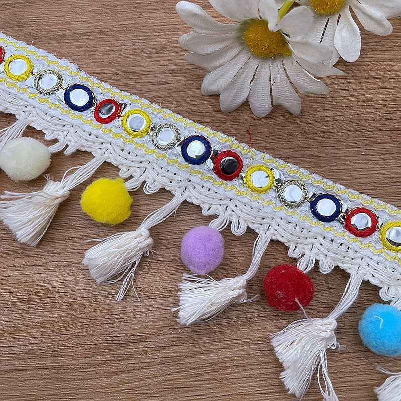 Colorful ring-embroidered border on white trim with fringe and small pom-poms.