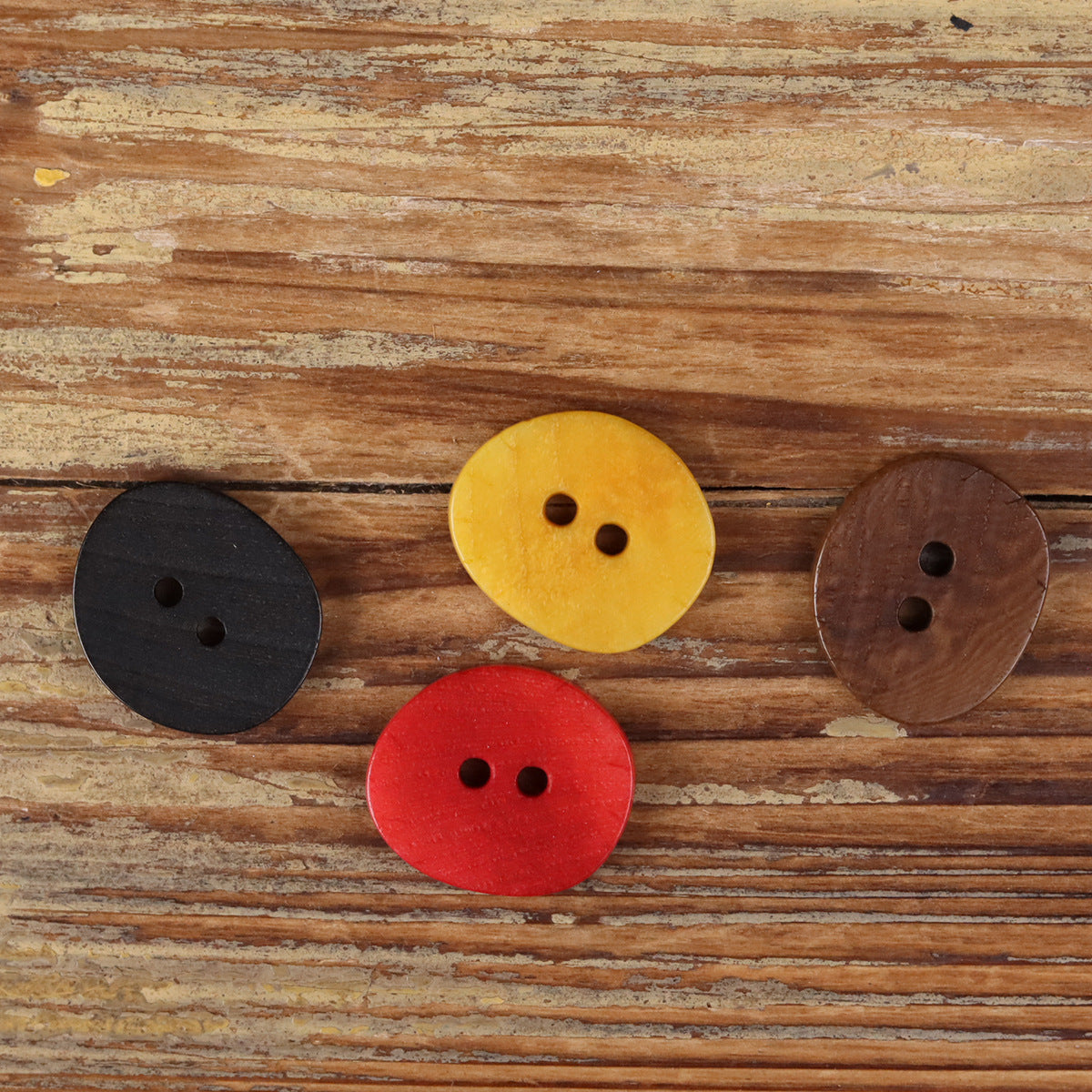 Assorted natural 2-hole buttons in black, yellow, brown, and red on wood.