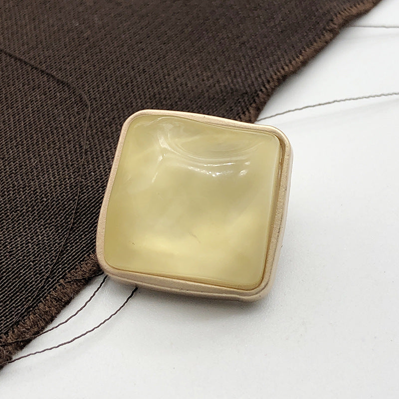 Square stone-look coat button, soft yellow, gold-tone metal shank, close-up