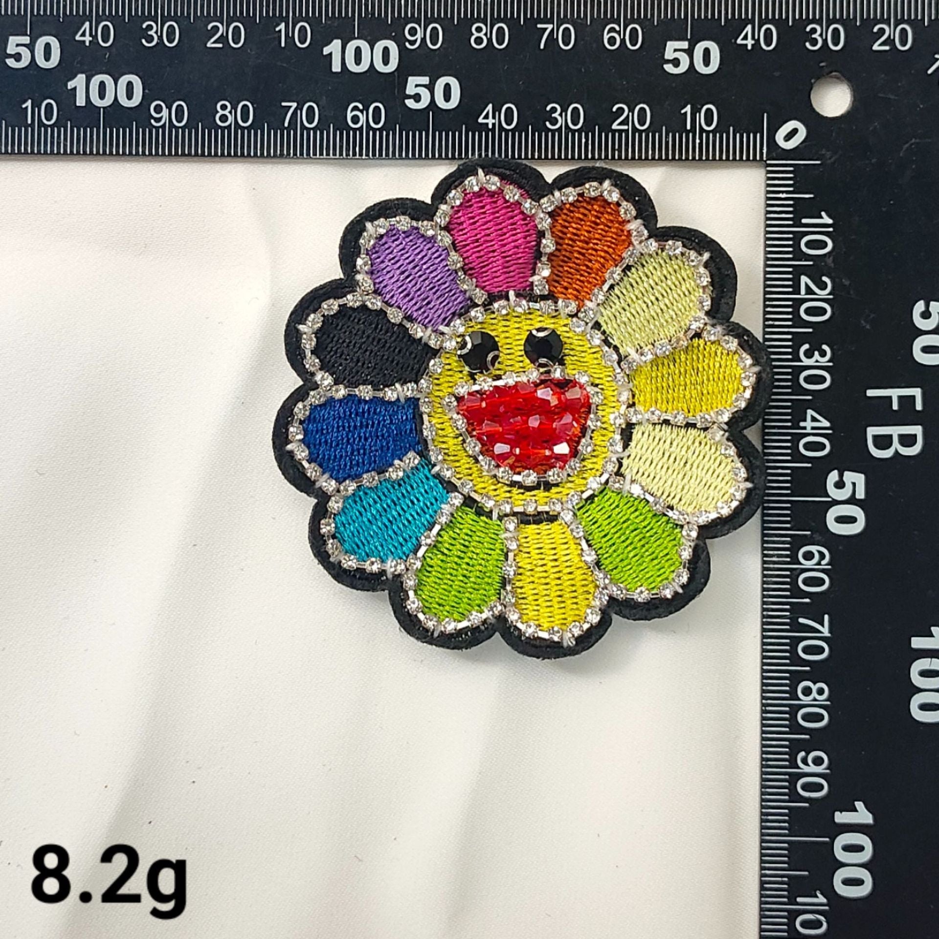 Parche bordado de girasol multicolor con cristal rojo central y acentos brillantes.
