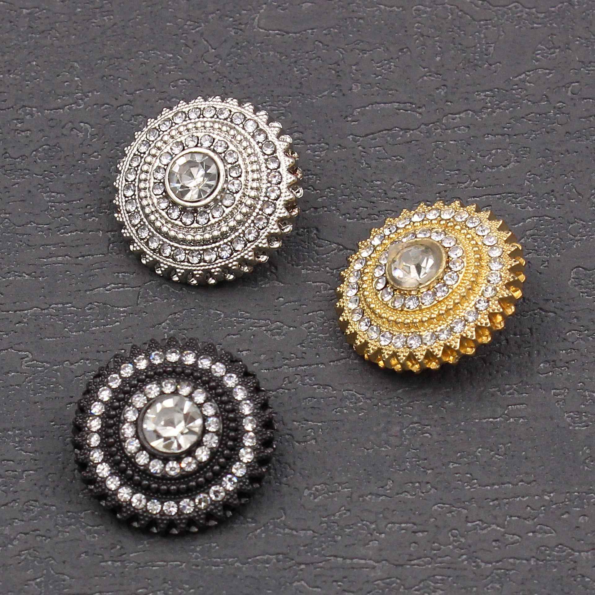Three round rhinestone buttons in silver, gold, and black with central crystal