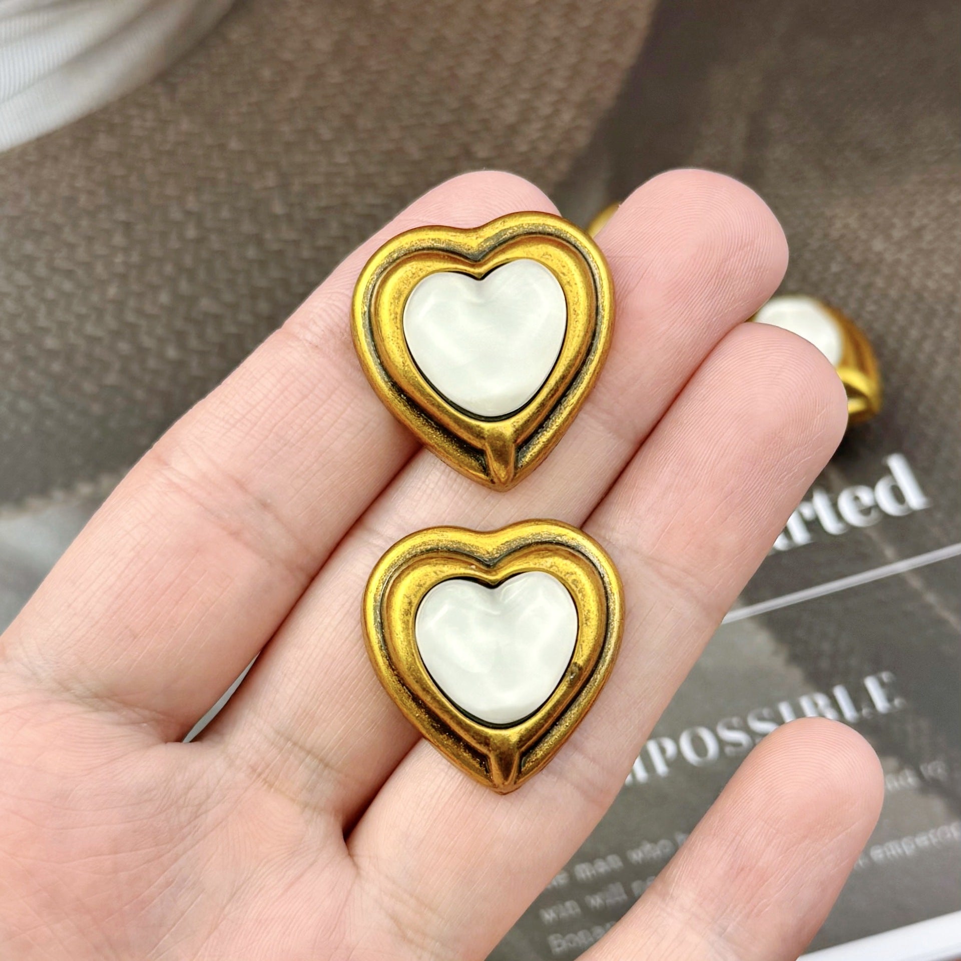 Two antique bronze heart metal shank buttons with white resin center, held in hand
