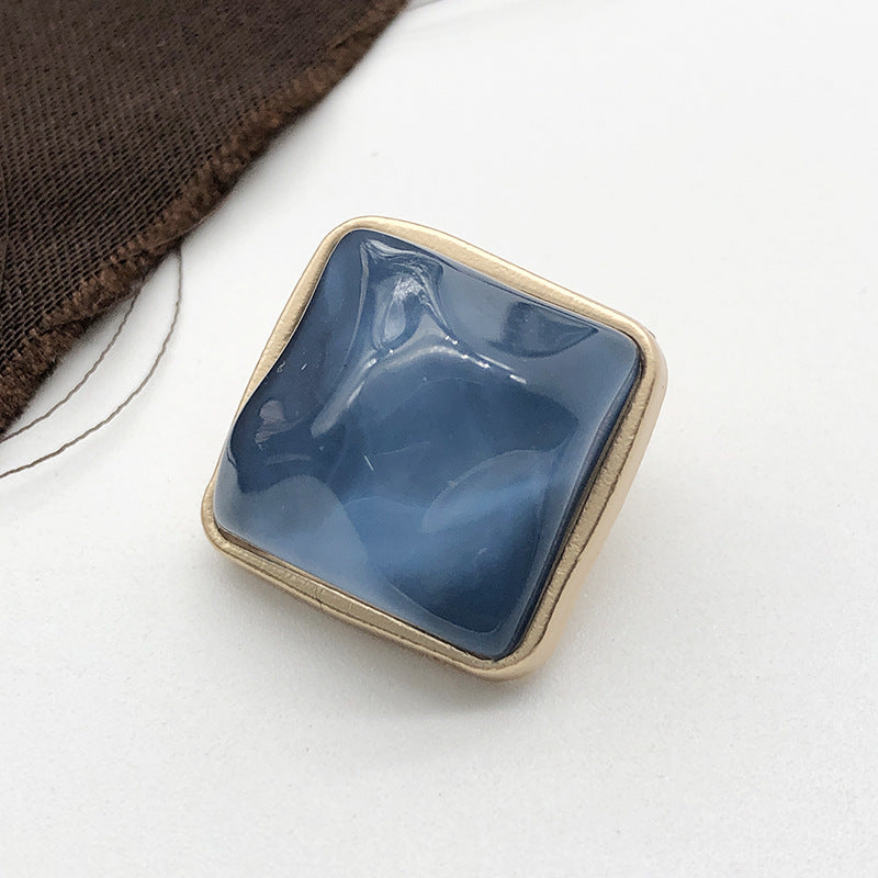 Square stone-look coat button, medium blue, gold-tone metal shank, close-up