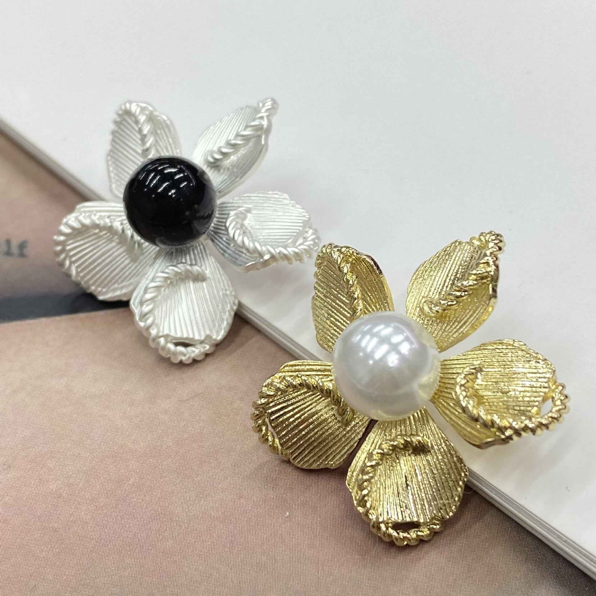 Two shank buttons: silver petals with black pearl, and gold petals with white pearl