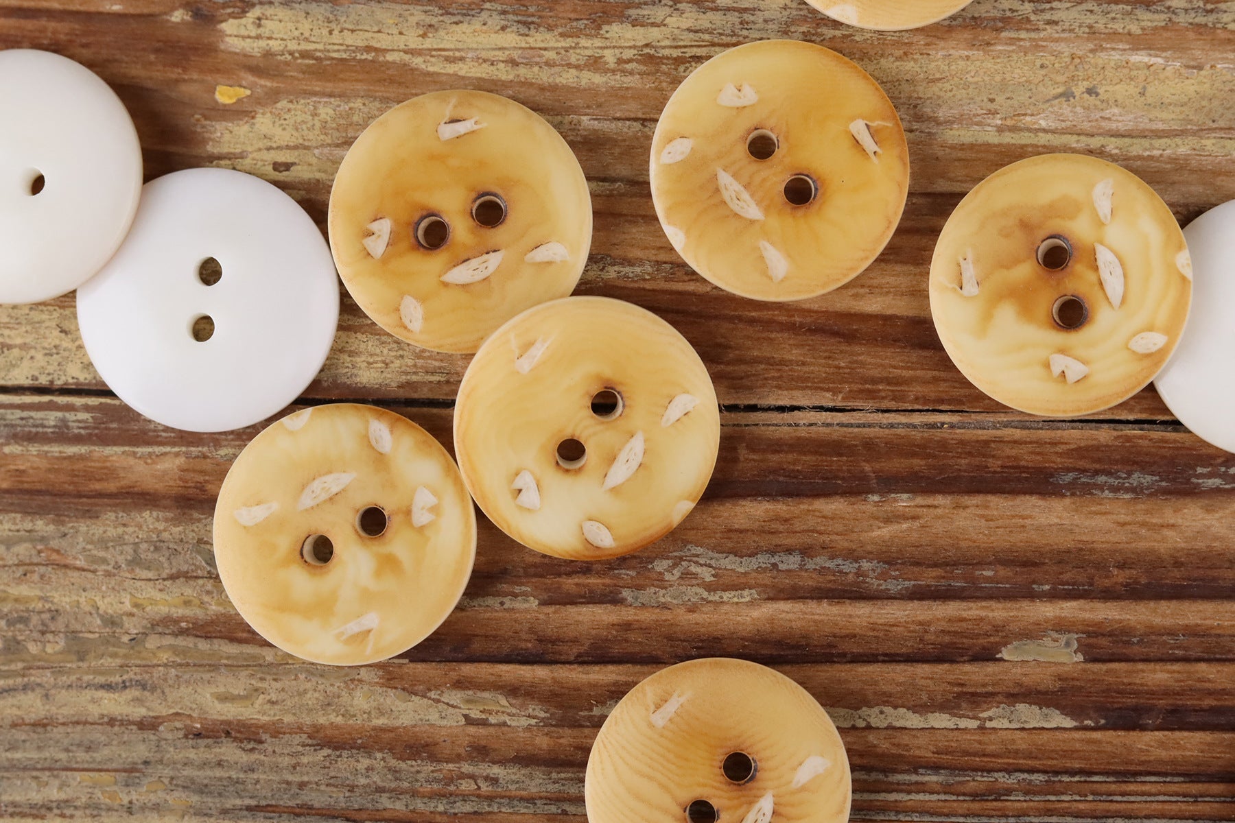 Round 2-hole buttons in pale cream and light golden tones with small printed marks