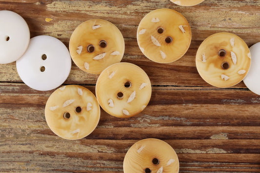 Round 2-hole buttons in pale cream and light golden tones with small printed marks