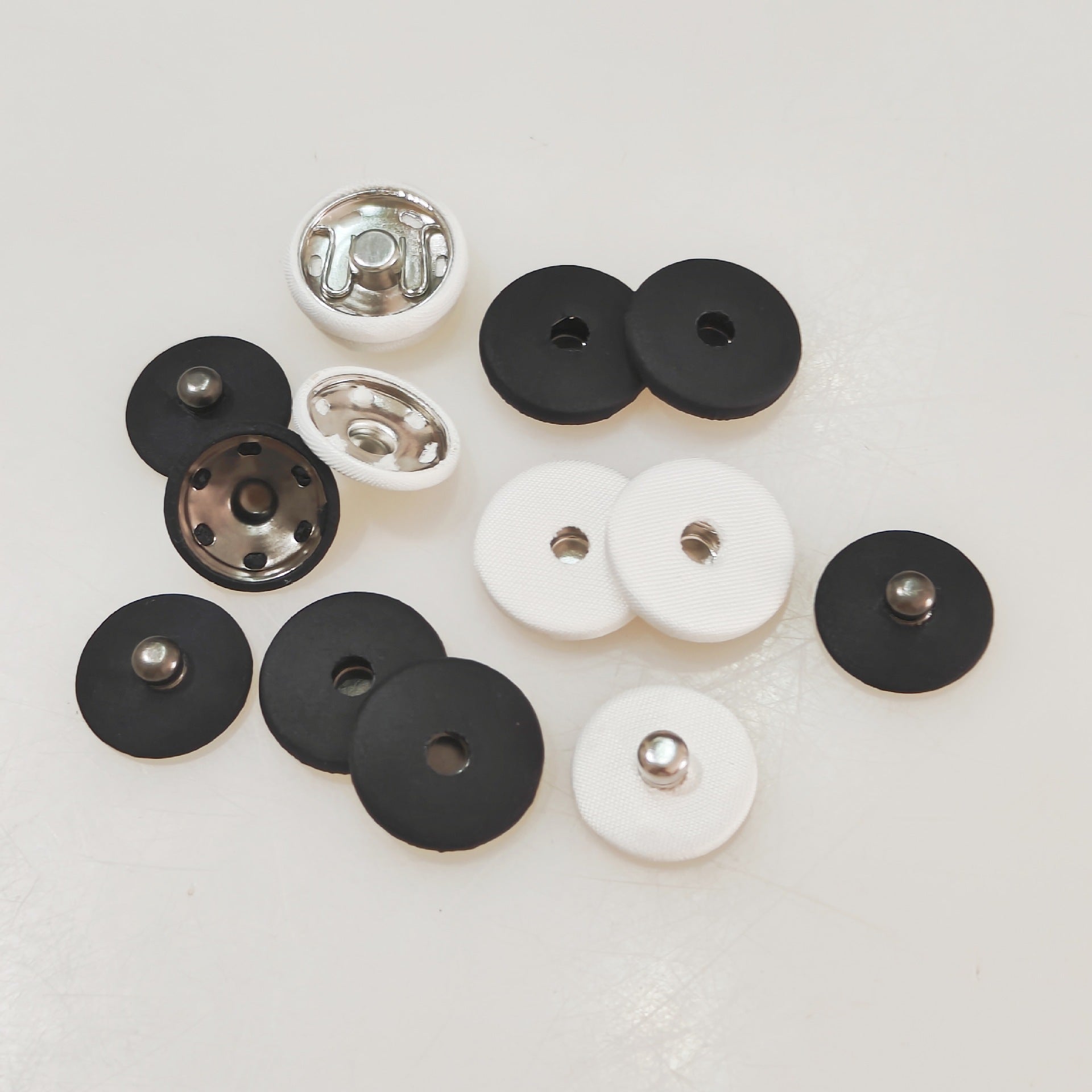 Mixed white and black fabric-covered invisible snap buttons with metal snap discs