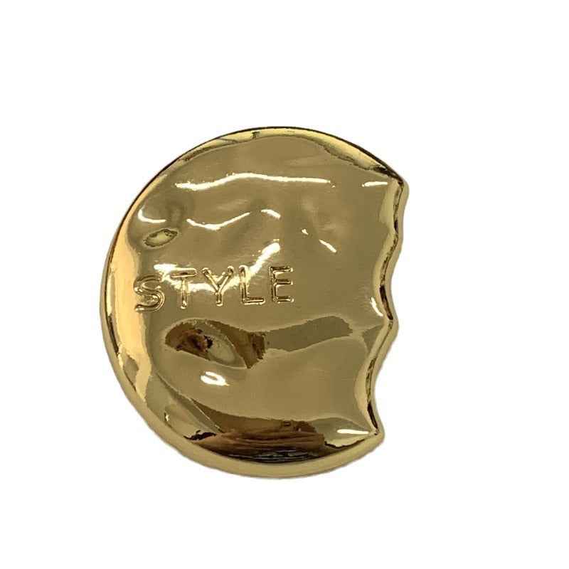 Gold semi-circular metal shank button close-up, engraved “STYLE” on face