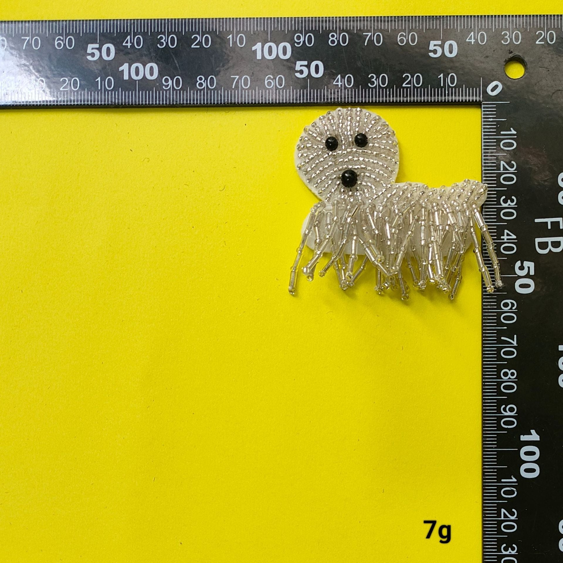 Small silver beaded dog patch with black bead eyes and long bead fringe, measured by ruler