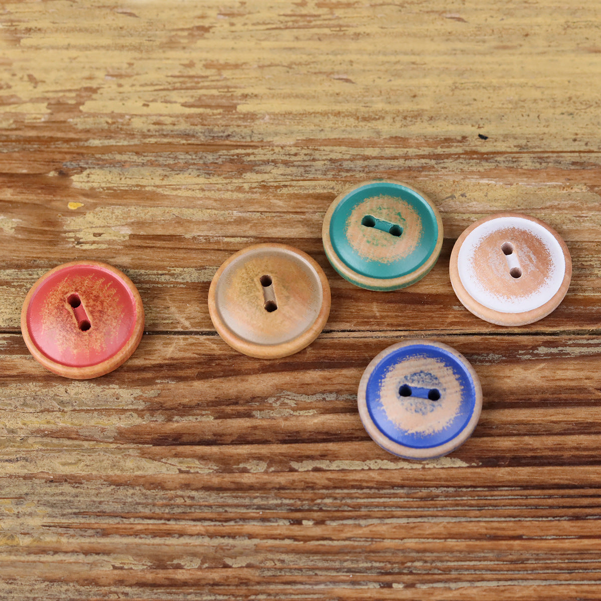 Round 2-hole wood buttons, assorted colors shown in a row on a wooden surface