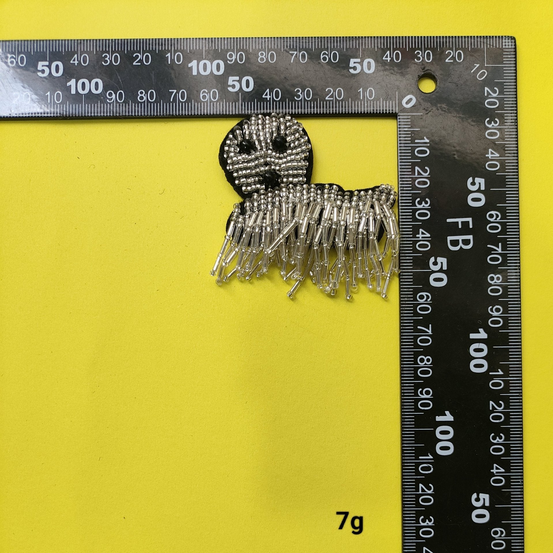 Silver beaded dog fabric patch with black bead eyes and dangling fringe, ruler scale
