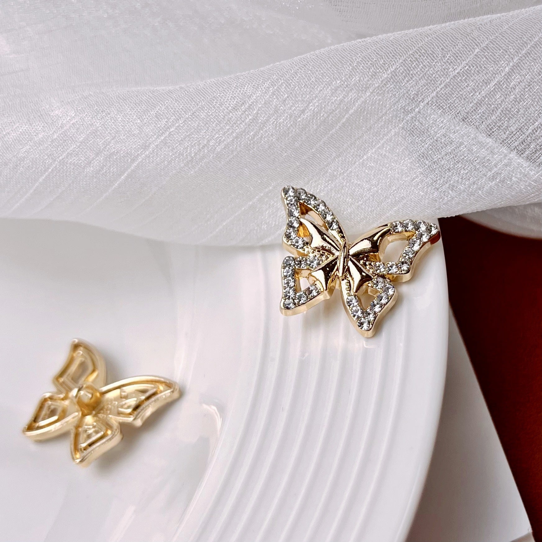 Rhinestone butterfly metal shank button on white coat fabric, gold-tone