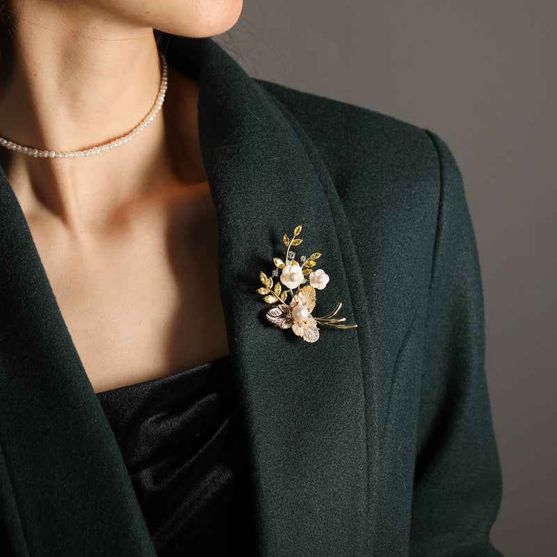 Flower brooch with white pearl cluster and gold-tone leaves pinned on dark blazer