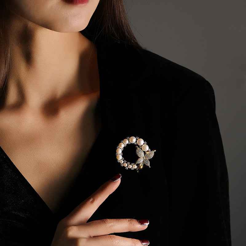 Goldfarbene Brosche mit Perlenkranz und Strass-Schmetterling am Revers