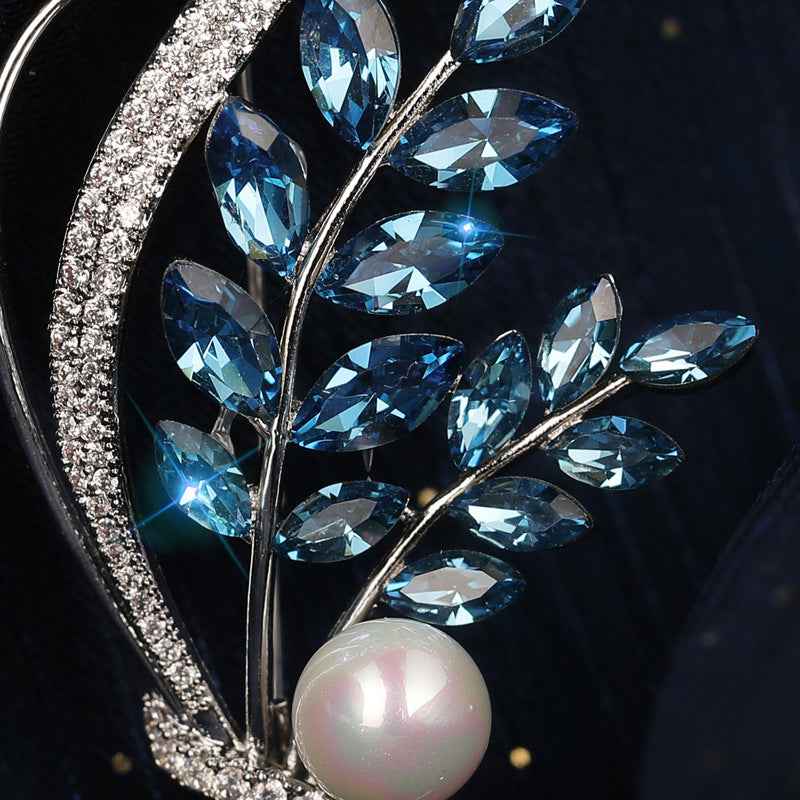 Close-up floral brooch with blue marquise crystals and a white freshwater pearl on silver frame.